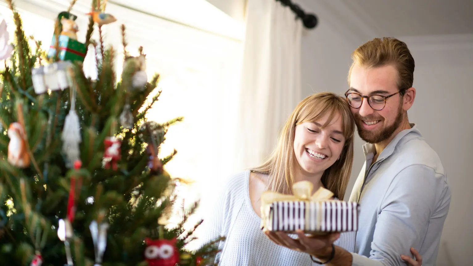 Couple with present next to Christmas tree