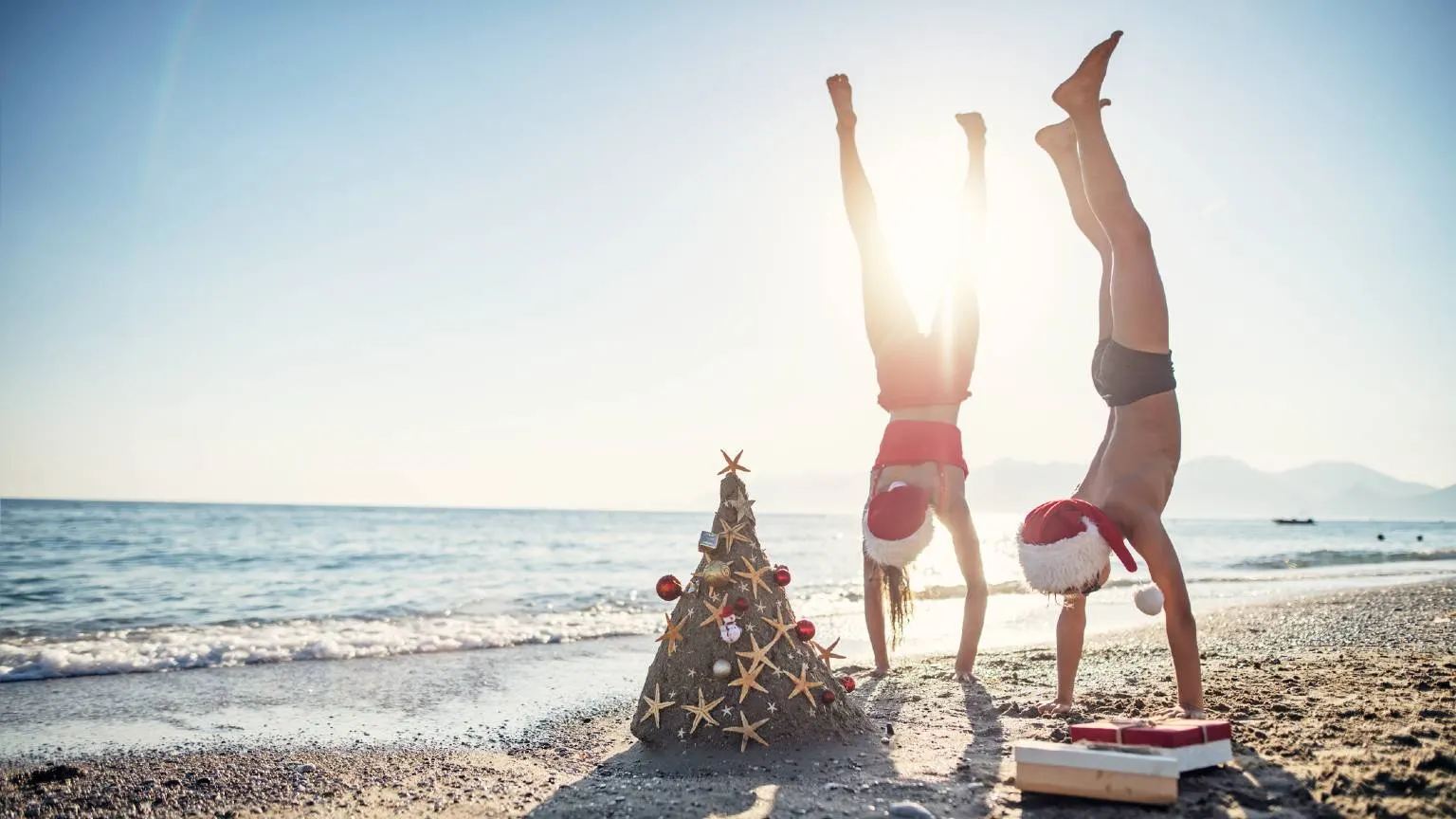 Brother and sister are having fun during summer Christmas. Kids are making handstands near the sand Christmas tree. 