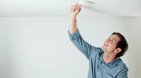 Young man testing smoke alarm on ceiling