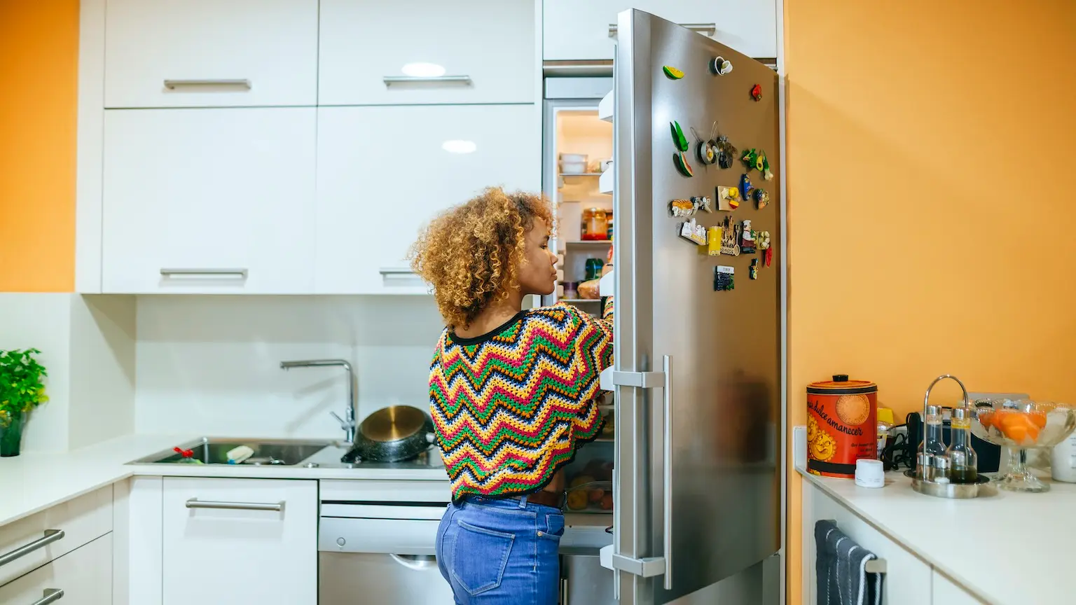 Young woman with curly hair opening the fridge in kitchen