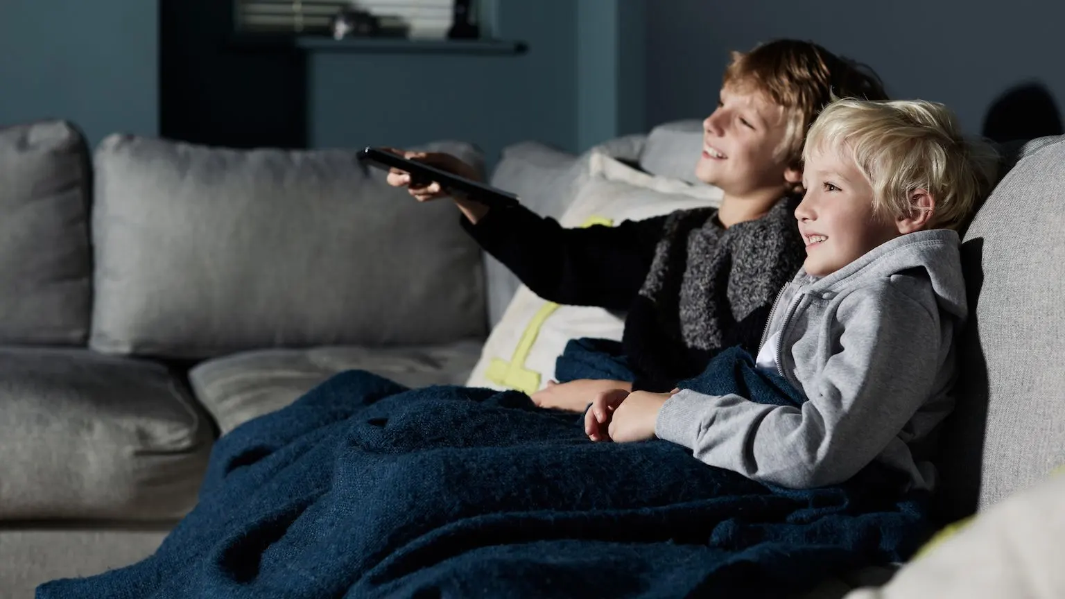 Two kids watching TV on a couch.