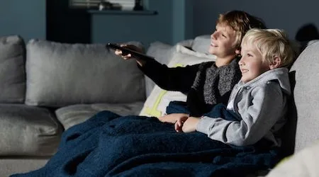 Two kids watching TV on a couch.