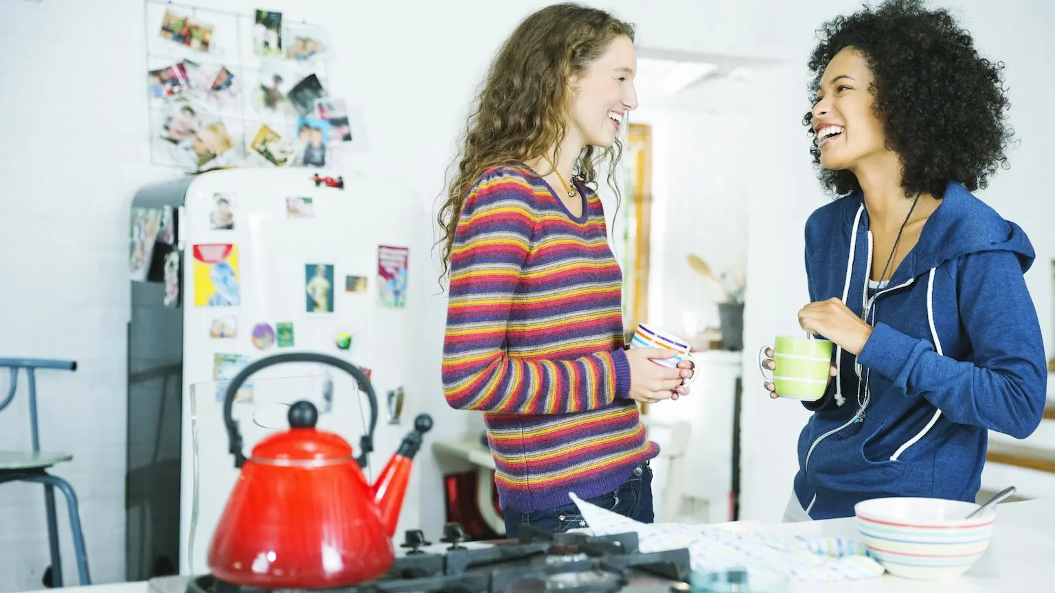 Two women talking and laughing while waiting for water to boil in a kettle.