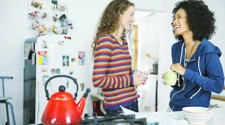 Two women talking and laughing while waiting for water to boil in a kettle.