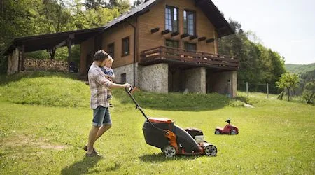 Man moving the lawn while holding his son.
