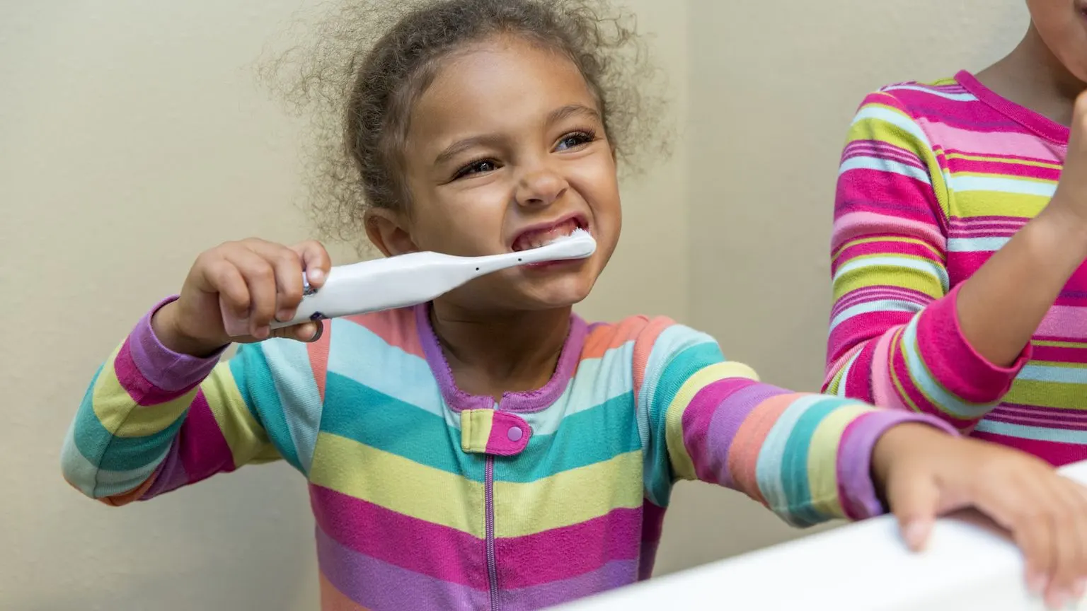 A little girl in bright pyjamas brushing her teeth in front of a mirror
