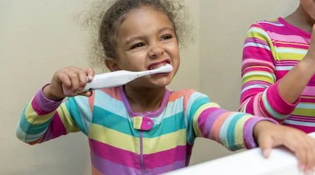 A little girl in bright pyjamas brushing her teeth in front of a mirror
