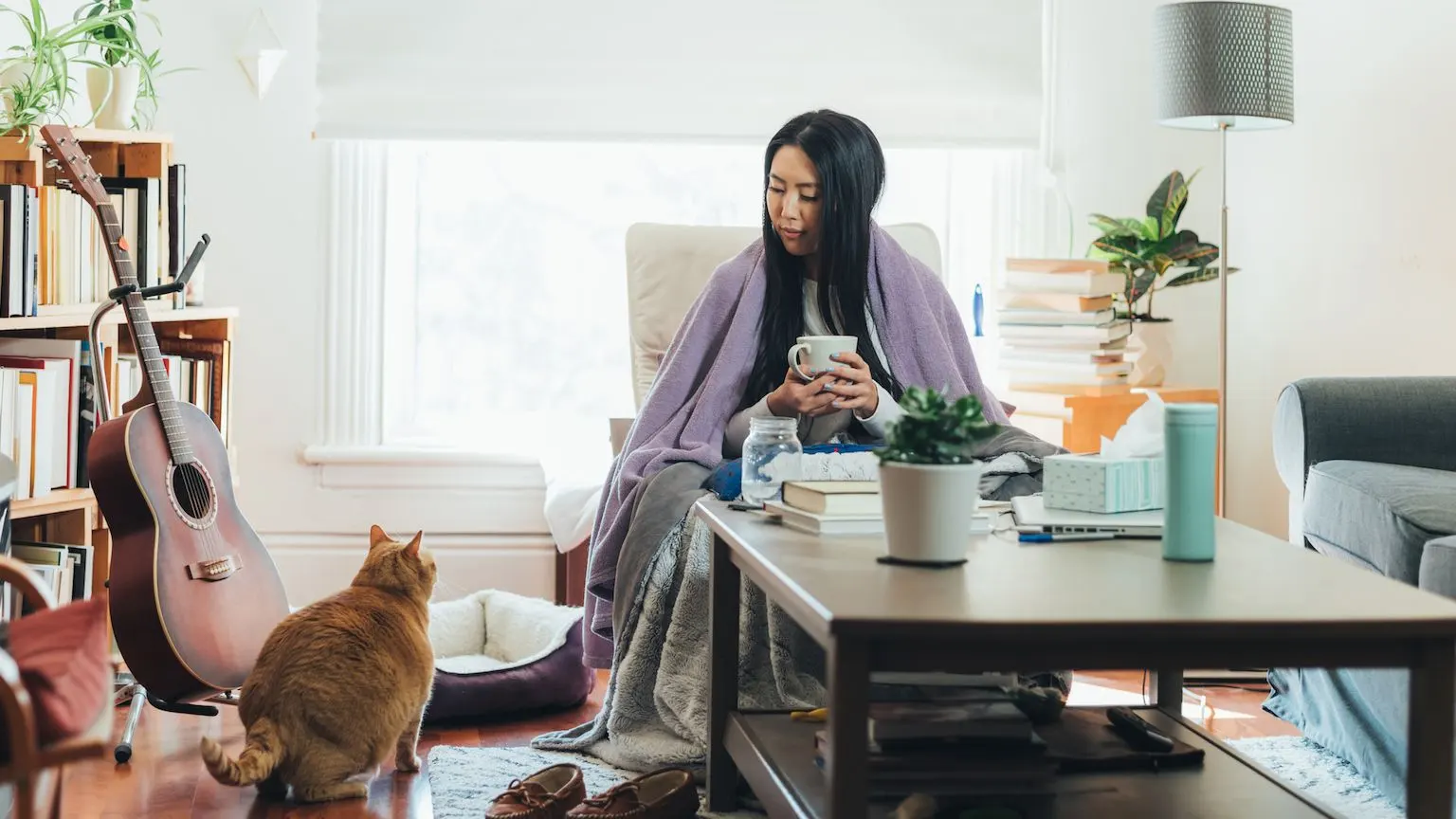 Woman warming up under a blanket with her cat and a cup of tea