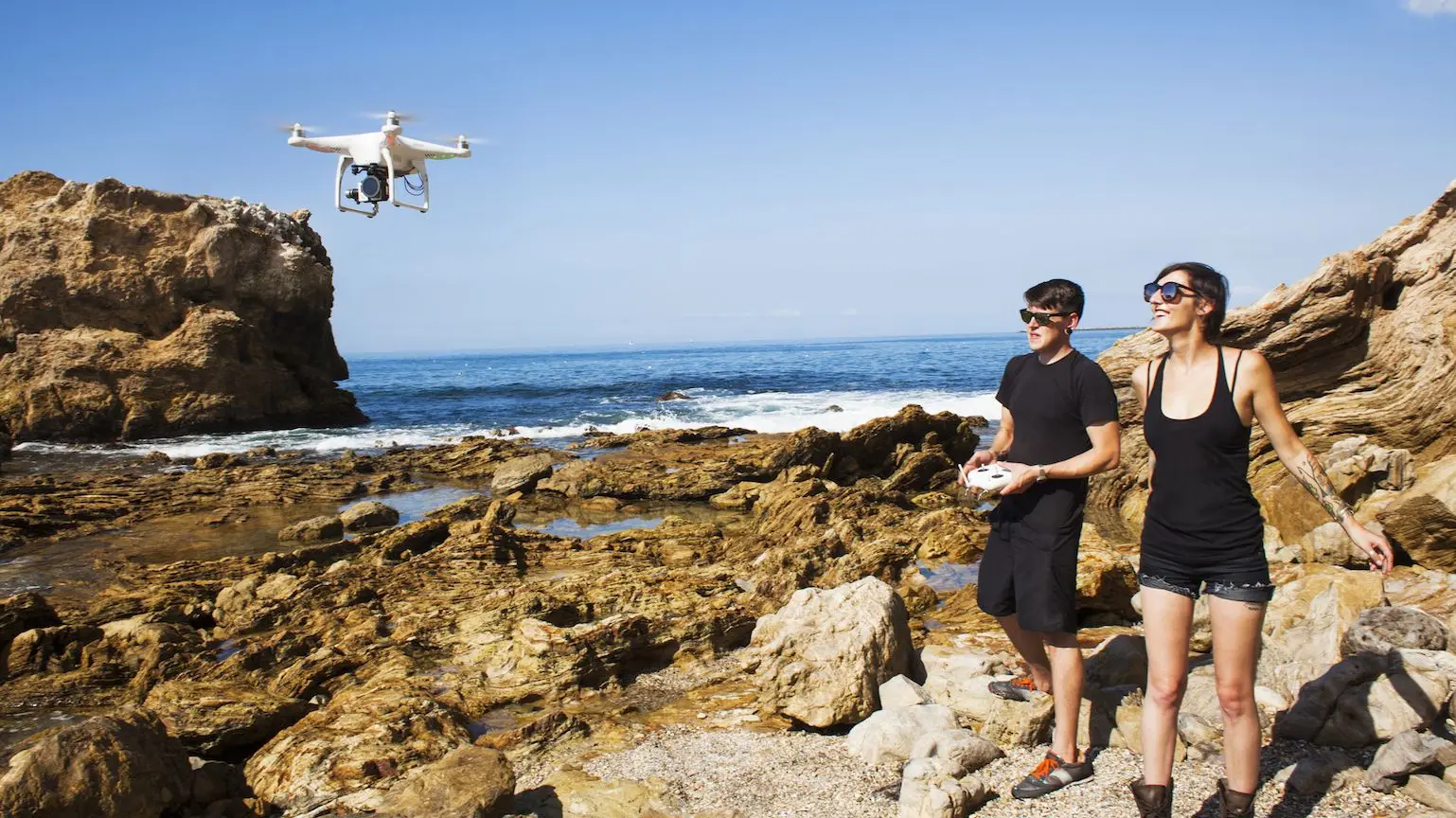 A young couple flying a drone at a rocky beach