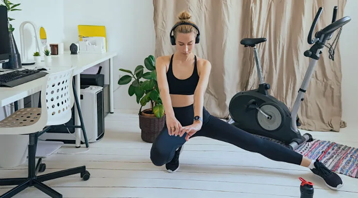 Image: Getty Images Woman stretching at home with exercise bike in the background