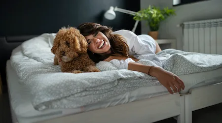 Young woman and her dog of apricot puddles meet in the morning in bed