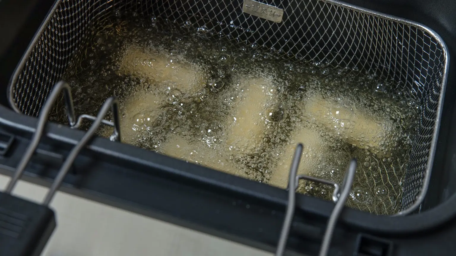 Potato croquettes being deep fried in deep fryer. Removable frying basket in 170 ÂºC oil. High point of view.