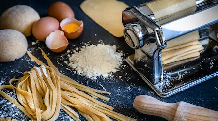 Front view of a homemade pasta machine surrounded by the ingredients for making pasta like eggs and flour. Low key DSLR photo taken with Canon EOS 6D Mark II and Canon EF 24-105 mm f/4L